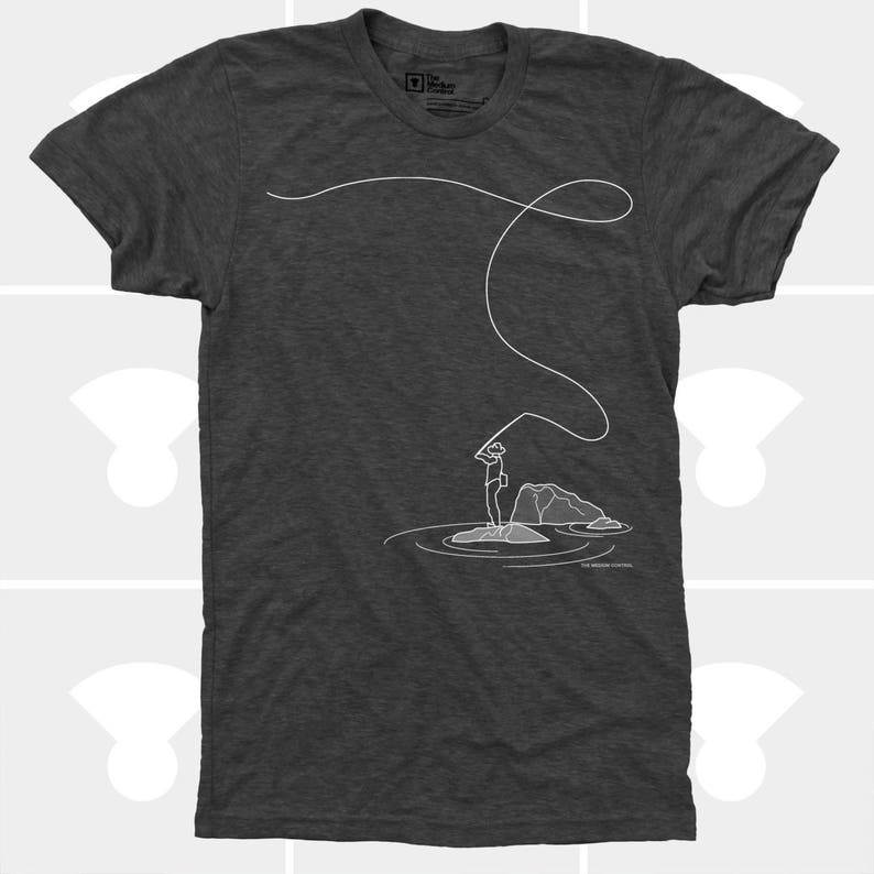 May include: Dark gray t-shirt featuring a minimalist white line drawing of a person fly fishing. The design includes a fishing rod, line, and a person standing on a rock in the water. The text "THE MISSION CONTROL" is at the bottom.