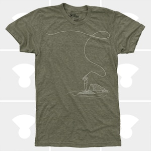 May include: Olive green t-shirt featuring a white line drawing of a person fly fishing. The illustration shows a person standing on a rock in the water, casting a line. The shirt has a crew neck and short sleeves.
