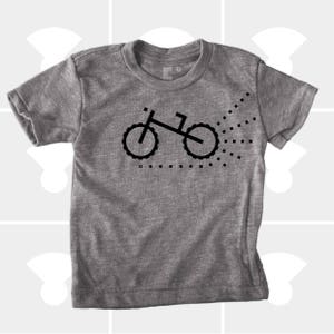 Puede incluir: Una camiseta gris jaspeada con una silueta negra de una bicicleta con un rastro de puntos detr&aacute;s.