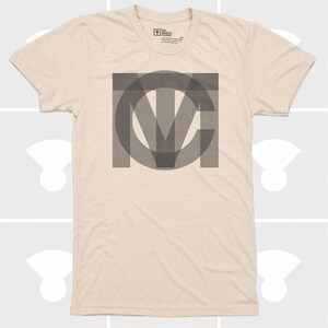 Pu&ograve; includere: T-shirt beige con una grande grafica grigia sovrapposta delle lettere "MCV". La maglietta ha maniche corte e girocollo. Il logo Medium Control &egrave; visibile in alto.
