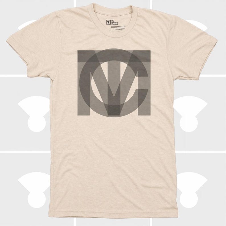 Pu&ograve; includere: T-shirt beige con una grande grafica grigia sovrapposta delle lettere "MCV". La maglietta ha maniche corte e girocollo. Il logo Medium Control &egrave; visibile in alto.