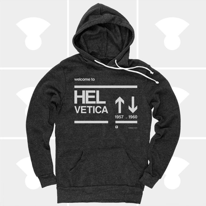 K&ouml;nnte beinhalten: Ein dunkelgrauer Kapuzenpullover mit einem wei&szlig;en Grafikdruck, auf dem "welcome to HELVETICA 1957 - 1960" mit nach oben und unten zeigenden Pfeilen steht.