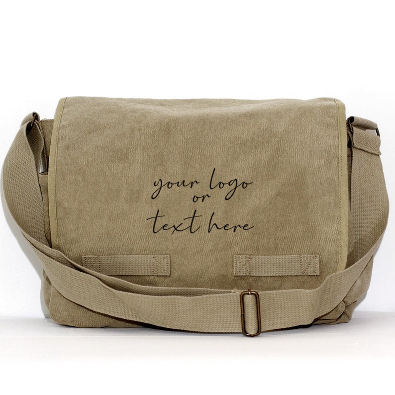 May include: A tan messenger bag with a flap closure and adjustable shoulder strap. The bag features the text "your logo or text here" in black script on the front. The bag has a rectangular shape and a buckle closure.