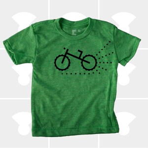 Puede incluir: Una camiseta verde de manga corta con un gr&aacute;fico negro de una bicicleta con un rastro de puntos detr&aacute;s.