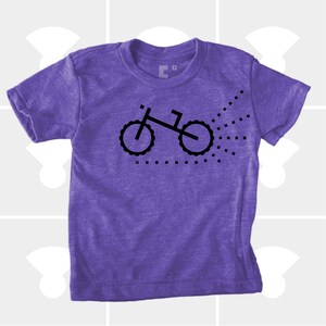 Puede incluir: Camiseta de manga corta de color morado con un gr&aacute;fico negro de una bicicleta con un rastro de puntos detr&aacute;s.