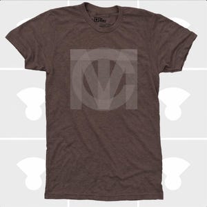 Pu&ograve; includere: T-shirt marrone girocollo con logo bianco sbiadito sul davanti. La maglietta &egrave; realizzata in un tessuto morbido e strutturato. Il logo sembra essere le iniziali "MCV" o "MVC" in un design stilizzato. La maglietta ha maniche corte.