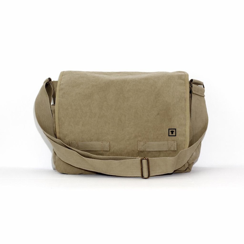 Front view of a blank khaki canvas messenger bag with a minimalist black square logo and antique brass hardware against a white background.