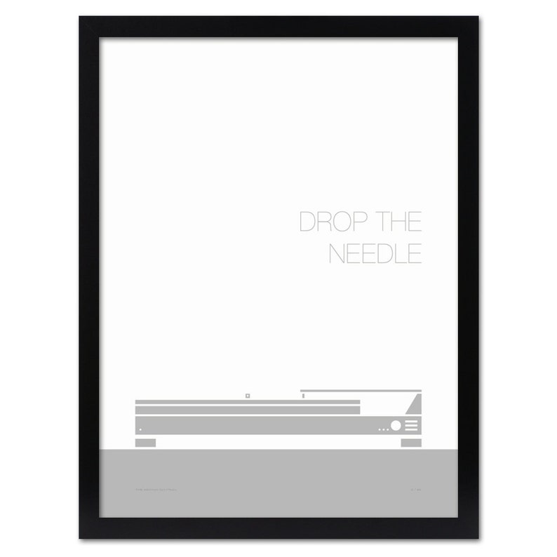 May include: A framed print with a minimalist design. The artwork features a gray illustration of a record player with the text "DROP THE NEEDLE" in a light gray font. The print is set against a white background and framed in black.
