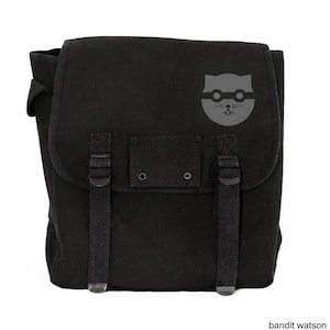 May include: Black messenger bag with a flap closure and adjustable straps. The bag features a gray graphic of a cat wearing glasses. The bag has a rectangular shape and is made of a durable fabric.