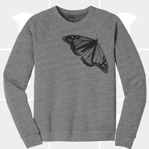 Op de afbeelding: Een grijs sweatshirt met een zwarte vlinderprint op de voorkant.