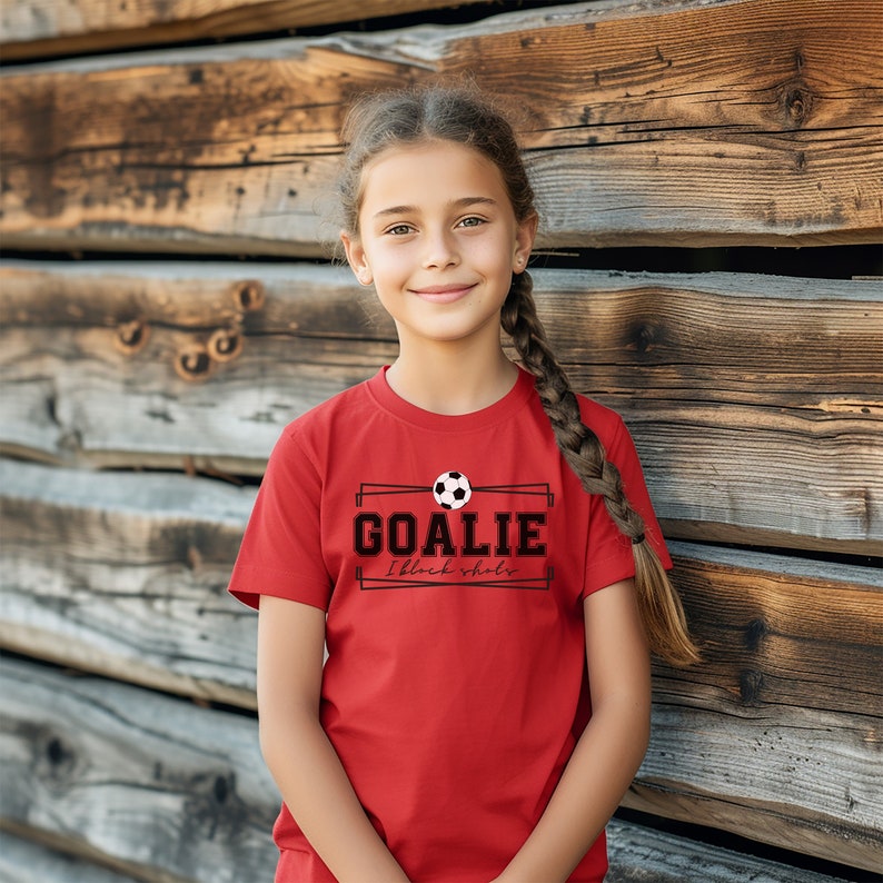 Puede incluir: Una camiseta roja con un gr&aacute;fico de bal&oacute;n de f&uacute;tbol en blanco y negro y el texto "GOALIE I block shots".
