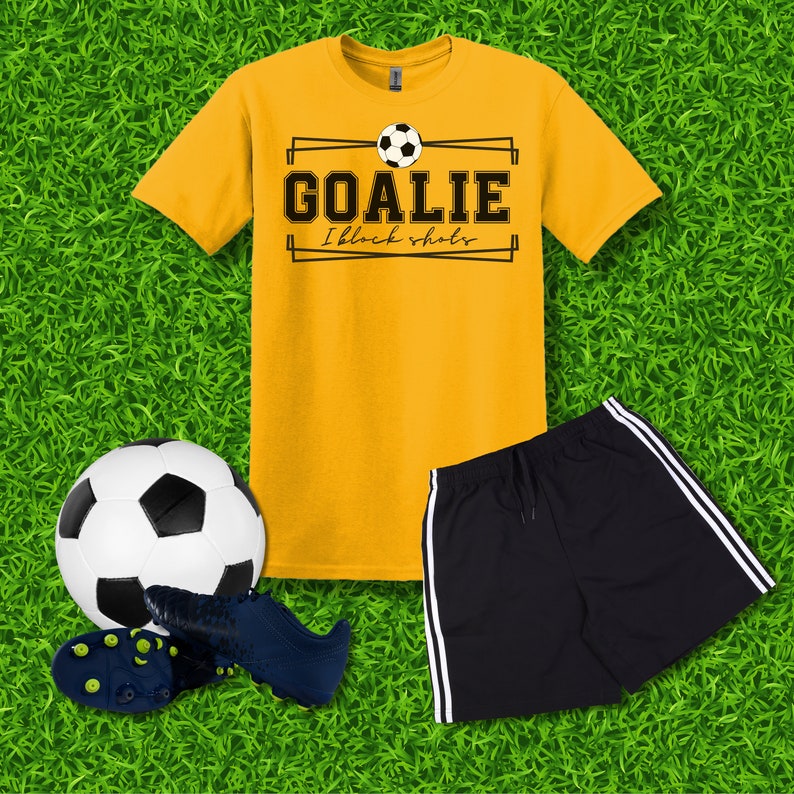 Puede incluir: Una camiseta amarilla con un gr&aacute;fico negro que dice "Goalie I block shots" con un bal&oacute;n de f&uacute;tbol sobre el texto. Un pantal&oacute;n corto deportivo negro con rayas blancas a los lados. Un bal&oacute;n de f&uacute;tbol blanco y negro y un par de botas de f&uacute;tbol negras.