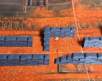May include: A set of five miniature gray sandbag barricades for tabletop gaming. The collection includes straight wall sections, an L-shaped corner piece, and a stepped barricade, all featuring a molded texture representing stacked fabric bags.