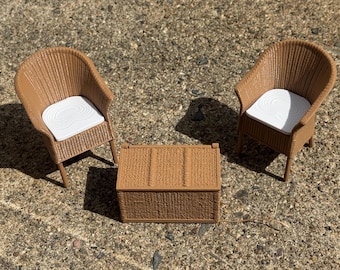 May include: A miniature furniture set consisting of two brown wicker-style chairs with white seat cushions and a matching rectangular brown wicker-style storage chest positioned between them, all featuring a textured, woven-look surface finish.
