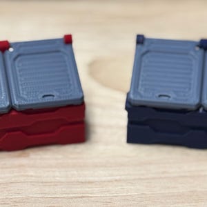 Peut inclure: Deux petites boîtes de rangement rectangulaires avec des couvercles à charnières. La boîte de gauche est rouge et la boîte de droite est bleue.