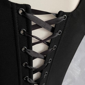 May include: Black corset with a lace-up back featuring black ribbon and metal eyelets.