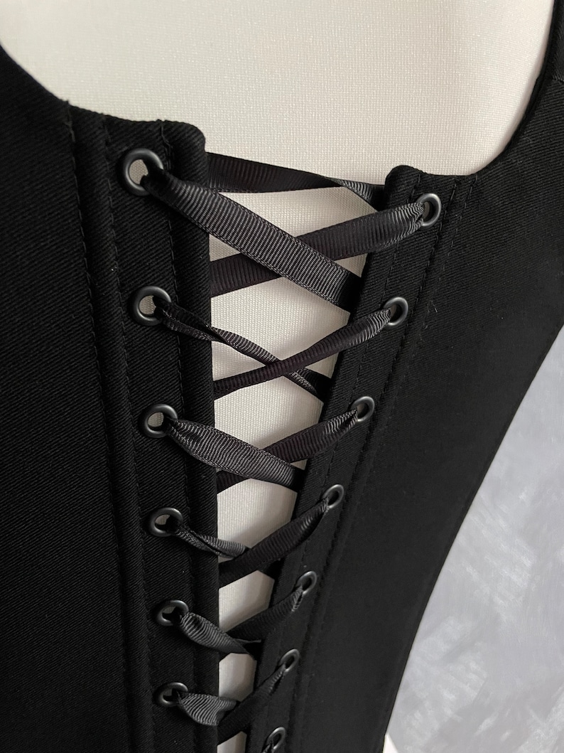 May include: Black corset with a lace-up back featuring black ribbon and metal eyelets.