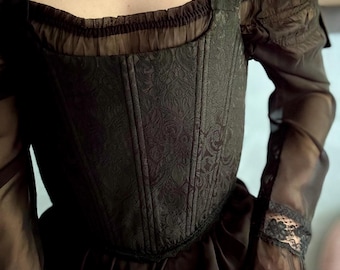May include: A black corset-style bodice featuring a tonal damask pattern, a square neckline with gathered sheer fabric, and long off-the-shoulder sheer sleeves with lace cuffs. A white pearl necklace is worn around the neck.