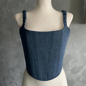May include: A blue denim corset top with adjustable straps. The top has a square neckline and is fitted to the body.