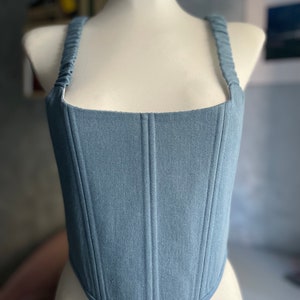 May include: A blue denim corset with adjustable straps. The corset has a pointed bottom and is made of a sturdy fabric.