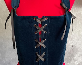 May include: A dark blue velvet corset with black ribbon lacing and straps. The corset has a square neckline and a pointed bottom.
