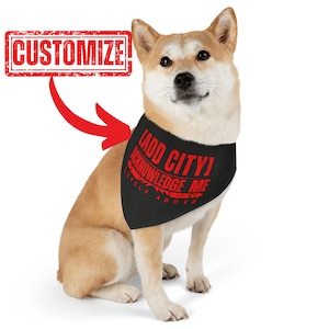 May include: A black dog bandana with red text that reads "LADD CITY! ACKNOWLEDGE ME LEVELS ABOVE". The bandana is worn by a light brown dog with a white chest.