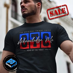 May include: Black t-shirt with the text "OTC Acknowledge Me Head of the Table" in blue, red, and white. The shirt also features the text "The Original Tribal Chief". A "SALE" stamp is in the upper right corner.