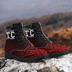 May include: A pair of black and red ankle boots with a tribal pattern. The boots have black laces, a black sole, and the letters "TC" in white on the top. The boots are sitting on a rock.