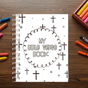 Può includere: Un quaderno a spirale con la scritta "MY BIBLE VERSE BOOK" circondata da croci ed elementi decorativi. Pennarelli colorati di vari colori sono sparsi intorno al quaderno su una superficie di legno.