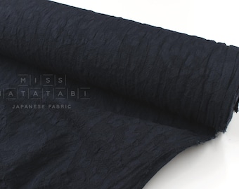 May include: A roll of dark navy blue fabric with a crinkled, textured surface. The fabric features a subtle, repeating pattern and is marked with the text MISS MATATABI JAPANESE FABRIC in a white, grid-like overlay on the left side of the roll.