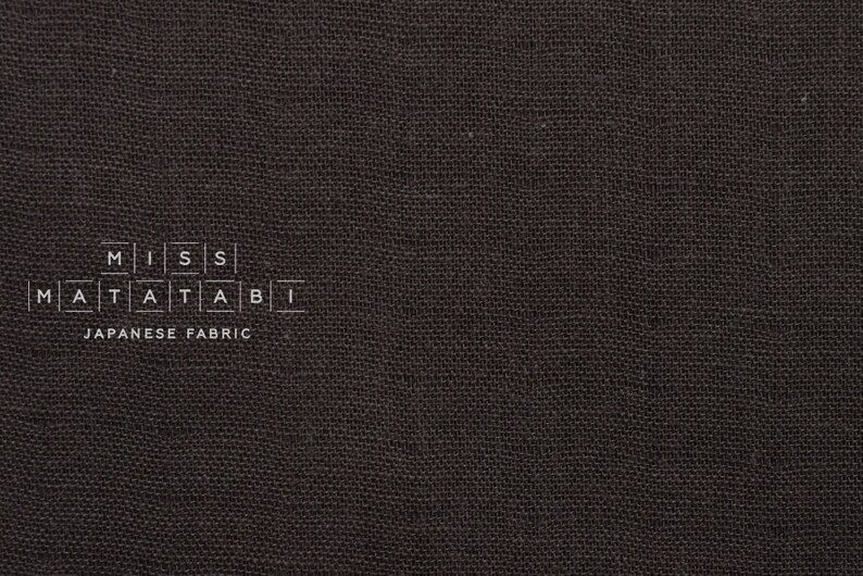 Puede incluir: Primer plano de una tela gris oscura con el texto "MISS MATATABI JAPANESE FABRIC" impreso en ella.