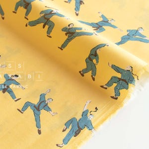 Könnte beinhalten: Gelber Stoff mit einem sich wiederholenden Muster aus blauen Figuren in Karate-Posen. Der Stoff trägt den Text "Miss Matatabi Japanese Fabric".