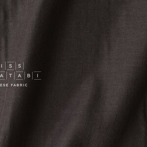 Puede incluir: Primer plano de una tela negra con una textura sutil. La tela tiene el texto "MISS MATATABI" y "JAPANESE FABRIC" impreso en ella.