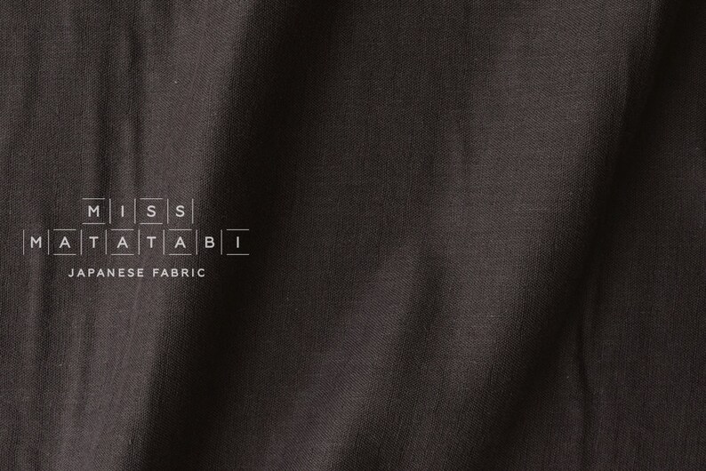 Puede incluir: Primer plano de una tela negra con una textura sutil. La tela tiene el texto "MISS MATATABI" y "JAPANESE FABRIC" impreso en ella.