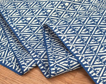 May include: Close-up of folded fabric with a repeating geometric pattern. The fabric has a navy blue background with a white diamond and floral design. The material is likely cotton or a similar fabric.