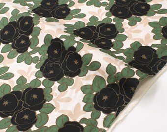 May include: Close-up of fabric with a repeating floral pattern. Black rose-like flowers with gold centers are surrounded by green leaves and beige accents on a white background. The fabric is folded, showing the edge.