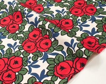 May include: Close-up of a fabric with a floral pattern. The design features clusters of red roses with black centers, green leaves, and blue accents on a cream background. The fabric is folded, revealing its edge.