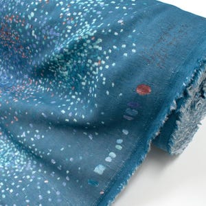 May include: A roll of blue fabric with a speckled pattern in white, teal, and orange. The fabric has a raw, unfinished edge. The pattern resembles a starry night or a scattering of confetti. Ideal for sewing and crafting projects.