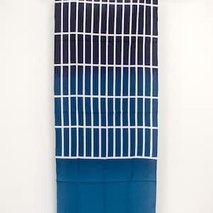 May include: A blue and white ombre fabric scarf with a grid pattern. The scarf is hanging from a branch.