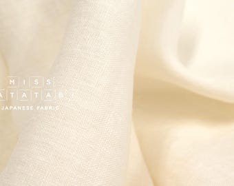 Puede incluir: Primer plano de una tela de lino de color blanco cremoso con una textura sutil. La tela está drapeada y doblada, mostrando su naturaleza suave y fluida. El texto "MISS MATATABI JAPANESE FABRIC" es visible en la esquina inferior izquierda.