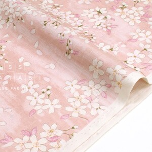 May include: Pink fabric with a white floral pattern of cherry blossoms. The fabric has a subtle texture and a light pink background. The text "MATATABI JAPANESE FABRICS" is visible in the lower left corner.
