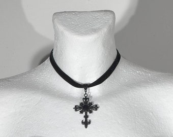 May include: A black velvet choker necklace with a large, ornate, black metal cross pendant.