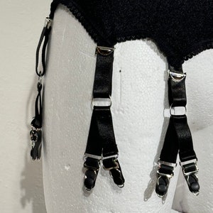May include: Black garter belt with four adjustable straps and metal clasps. The belt is made of a textured fabric with a scalloped edge. The straps are made of a shiny black material.