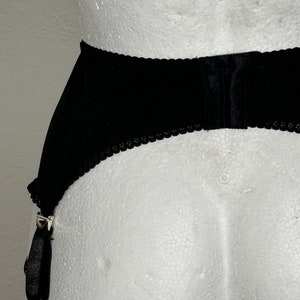 May include: Black garter belt with scalloped edges and adjustable straps. The belt is made of a soft, velvety material and features metal clasps for attaching stockings. The design is simple and elegant.