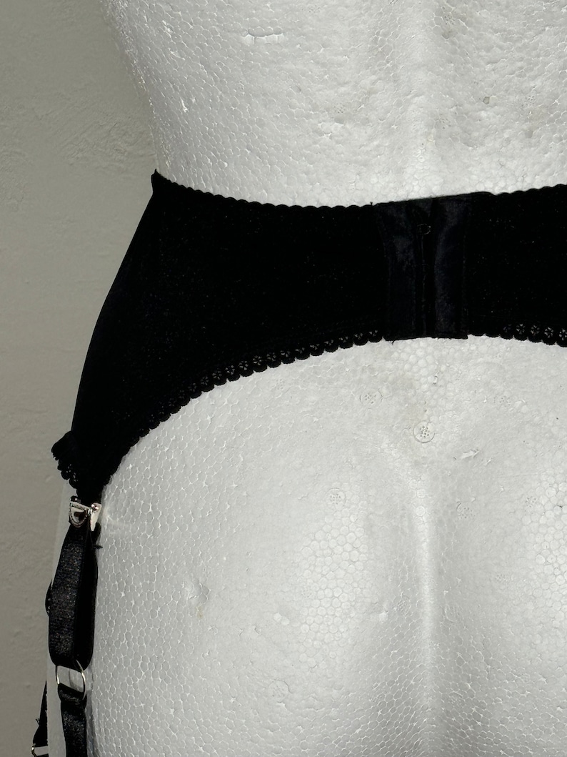 May include: Black garter belt with scalloped edges and adjustable straps. The belt is made of a soft, velvety material and features metal clasps for attaching stockings. The design is simple and elegant.