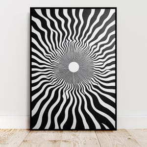 Peut inclure: Impression d'art abstrait en noir et blanc dans un cadre noir. L'œuvre présente un cercle blanc central entouré de lignes ondulées rayonnantes noires et blanches, créant une illusion d'optique. L'impression est exposée sur un sol en bois.