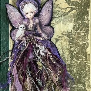 May include: A decorative wall hanging featuring a pale-skinned figure with white hair, large purple wings, and a small white owl. The figure wears a purple textured outfit with layered fabric strips, lace, and a metal key charm hanging at the waist.