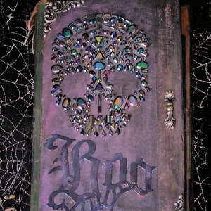 May include: A purple journal with a skull made of iridescent rhinestones and the word "Boo" written in black script.
