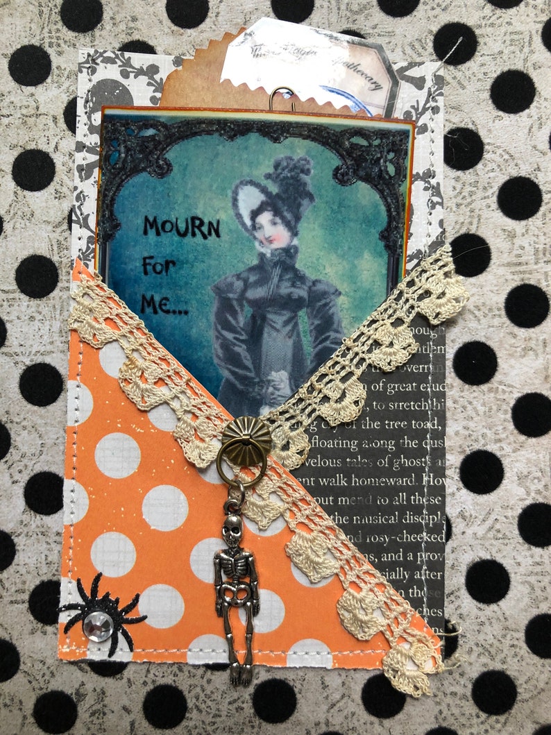 May include: A vintage-inspired Halloween card with a black and white image of a woman in a black dress and a white hat. The card is decorated with lace, polka dots, and a skeleton charm. The text on the card reads "MOURN For Me..."