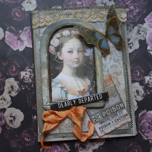 May include: A mixed media art piece featuring a portrait of a young girl with a floral crown, framed within a distressed, ornate border. A butterfly and orange ribbon add detail. The text "DEARLY DEPARTED" is visible.